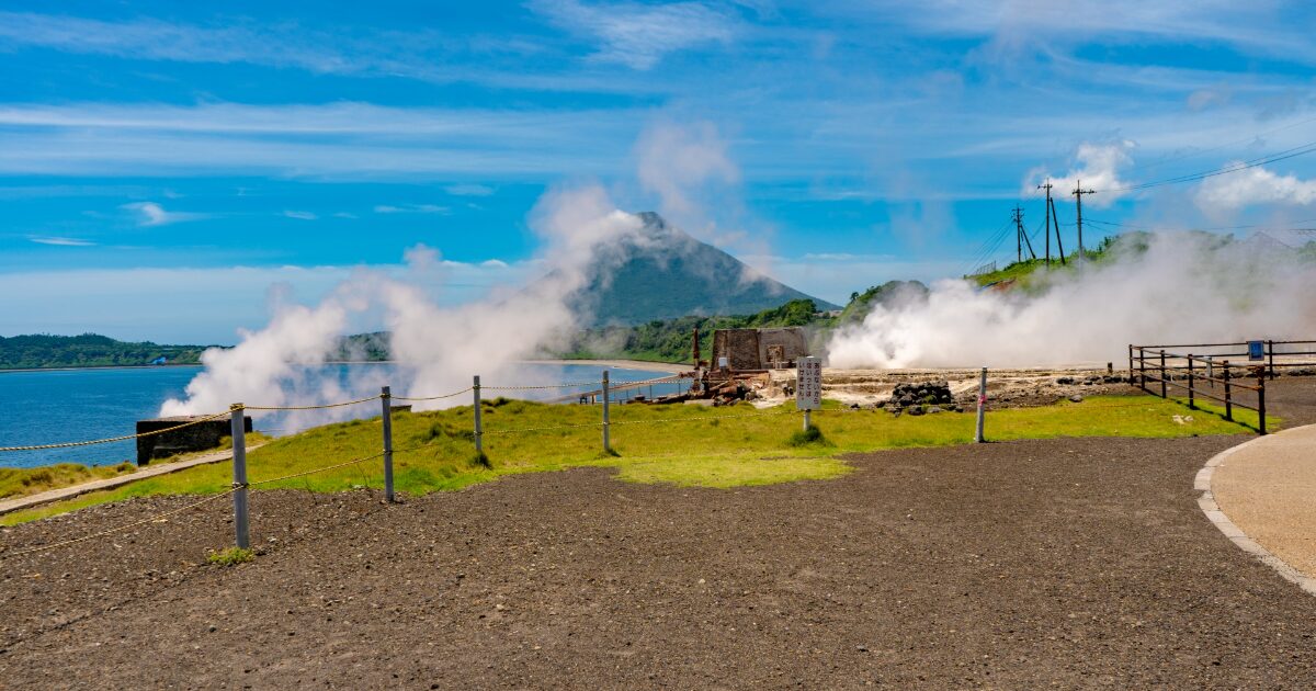 海辺の温泉地から噴き上がる湯気と開聞岳の景色