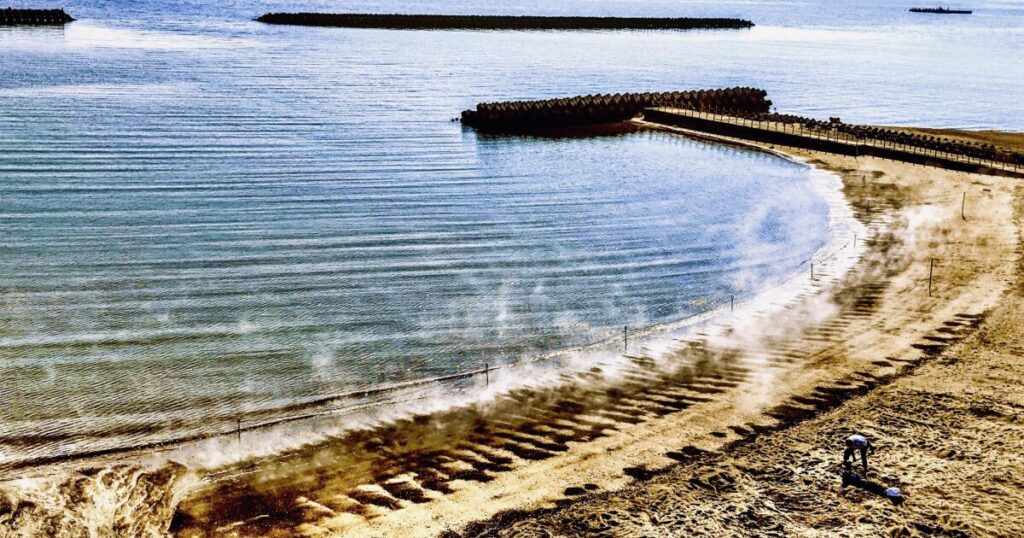 砂浜から立ち上る砂むし温泉の湯気と穏やかな海岸風景