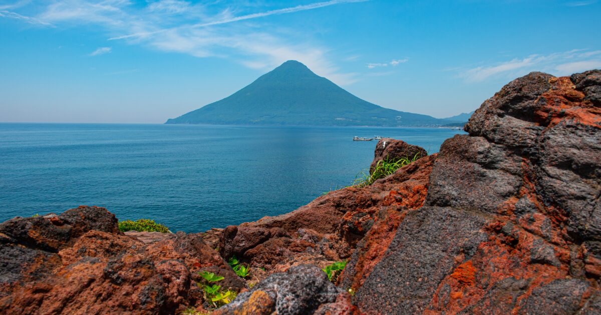 岩場の海岸越しに望む開聞岳と青い海の景色