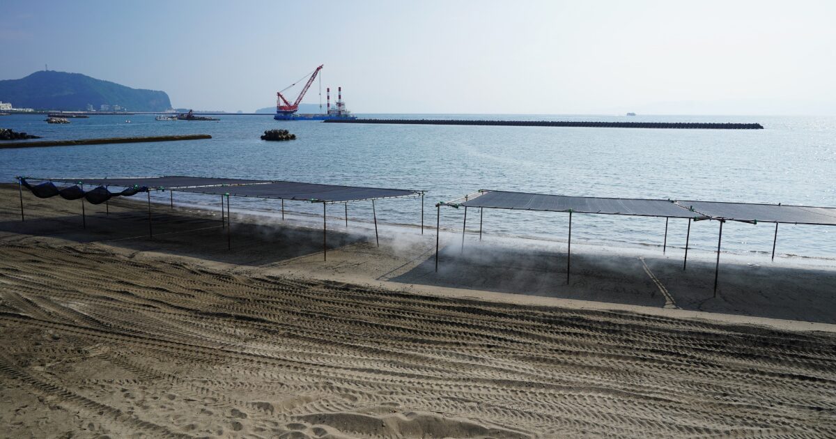海岸の砂浜と防波堤越しに見える穏やかな海の景色