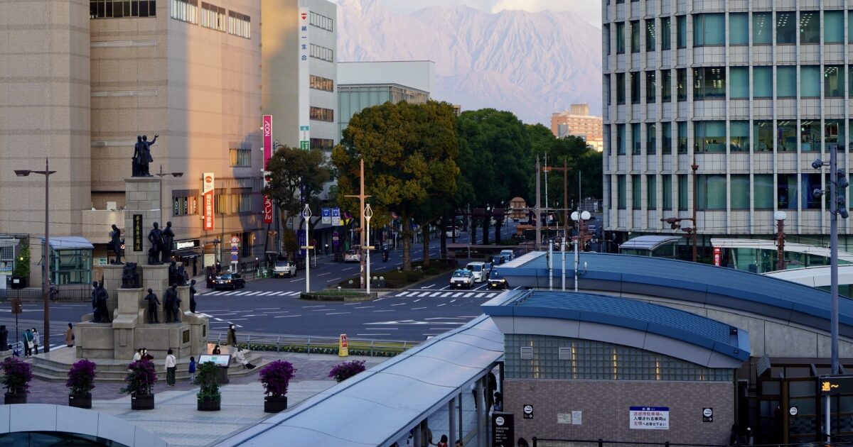 鹿児島市中心部の交差点とモニュメント越しの桜島風景