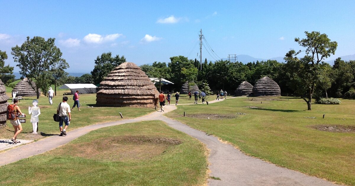 復元された竪穴式住居と来場者が歩く歴史公園
