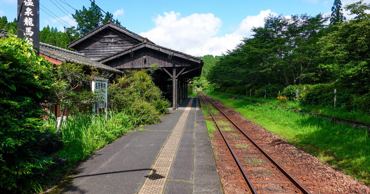 緑に囲まれた温泉地の木造駅と線路の風景