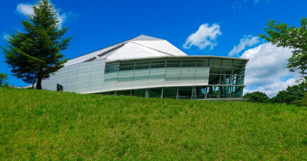 芝生の丘に建つ近代的なガラス張り建築の施設外観