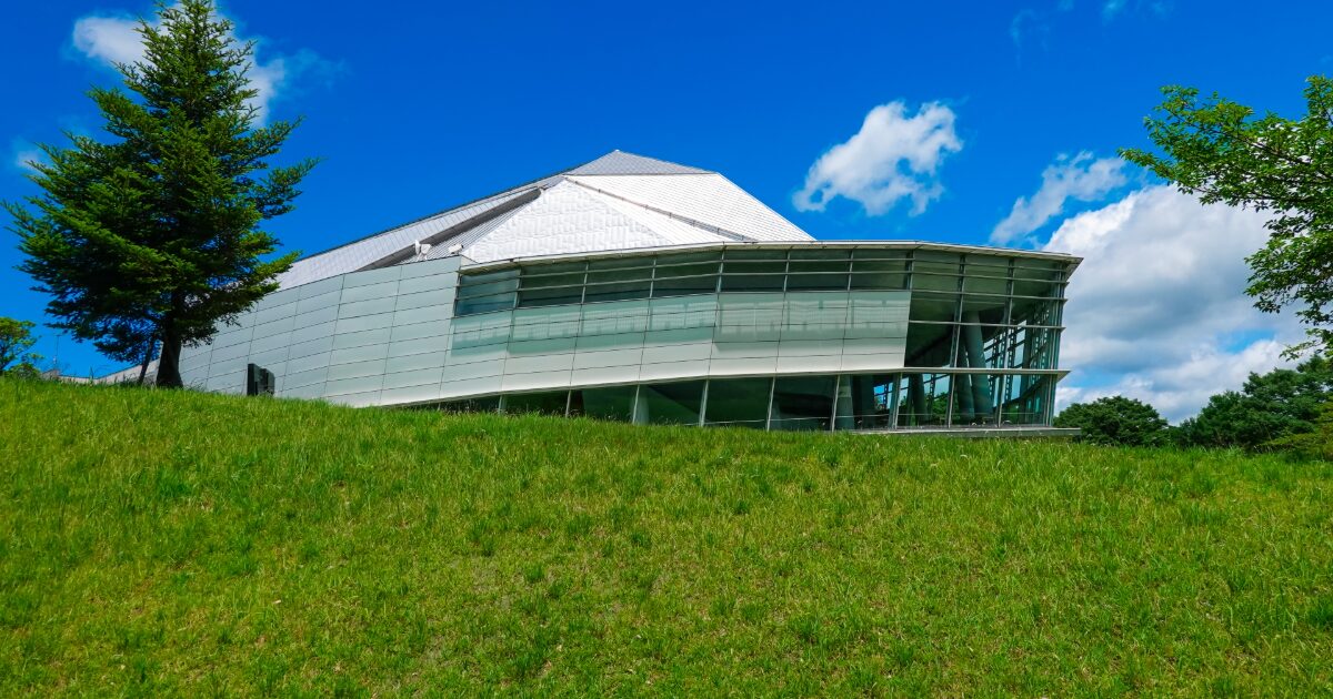 芝生の丘に建つ近代的なガラス張り建築の施設外観