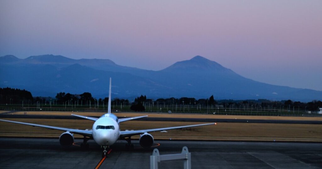 夕暮れの空港滑走路に停止する旅客機と山のシルエット