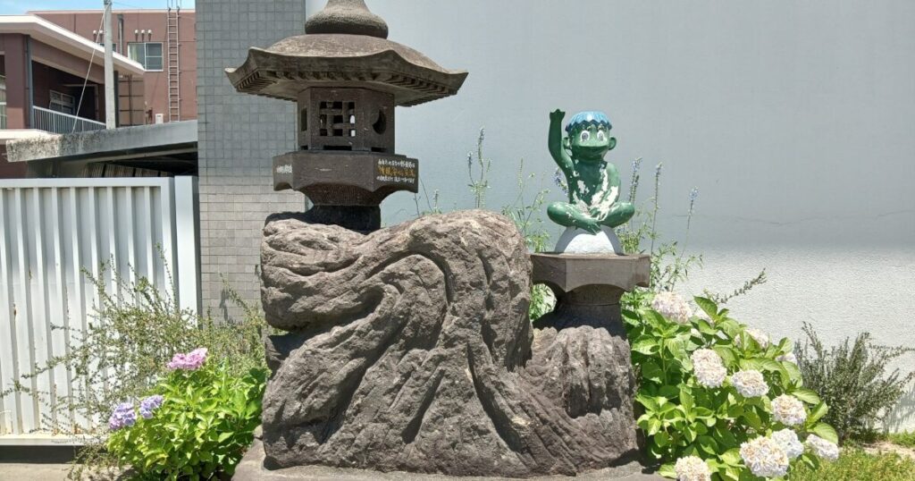 紫陽花の花に囲まれた石灯籠の横に座る河童の石像