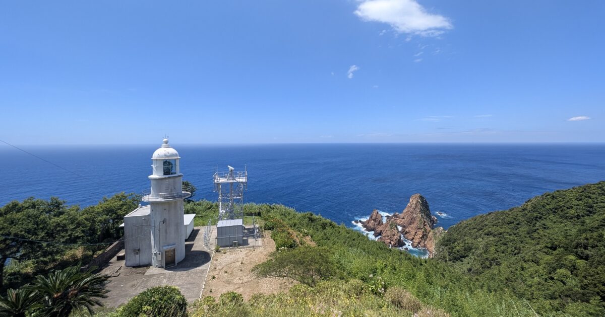 青空の下に立つ白亜の燈台と断崖絶壁の海岸線