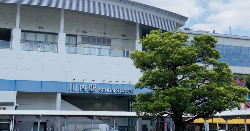 大きな街路樹越しに見る川内駅の駅舎正面