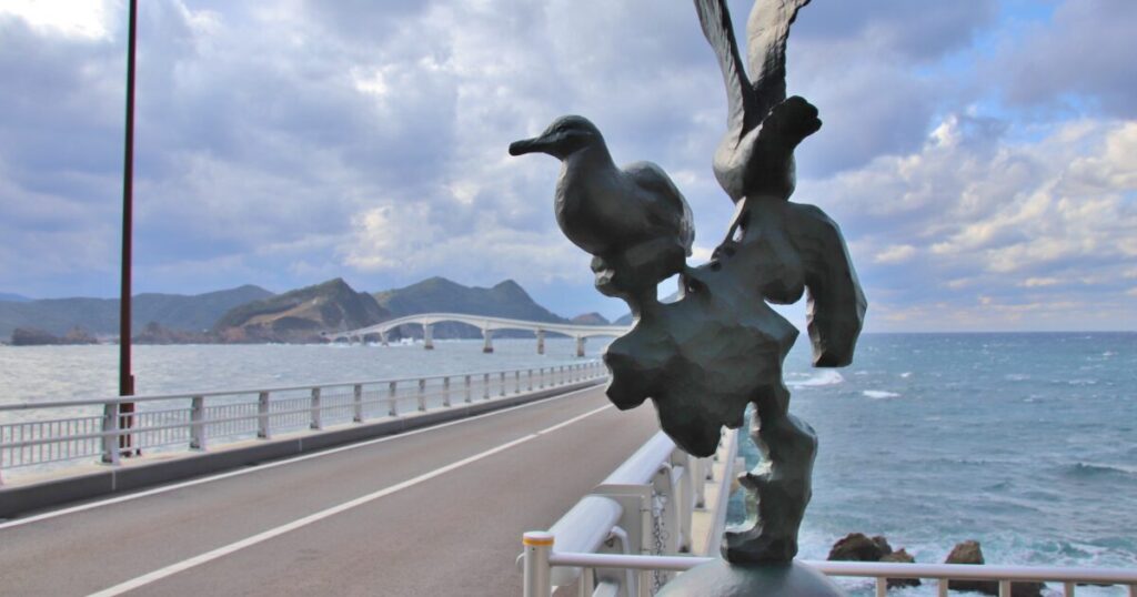 甑大橋の欄干に設置された鳥の彫刻と海へ続く道路